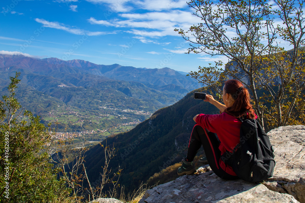 Woman trekker on the top of the mountain takes a photo of a landscape photo with a mobile phone