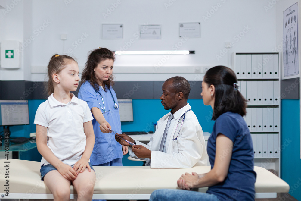 Obraz premium Therapist woman nurse giving lungs radiography to african american pediatrician doctor during child appointment in hospital office. Physician man explaining medical expertise. Health care service
