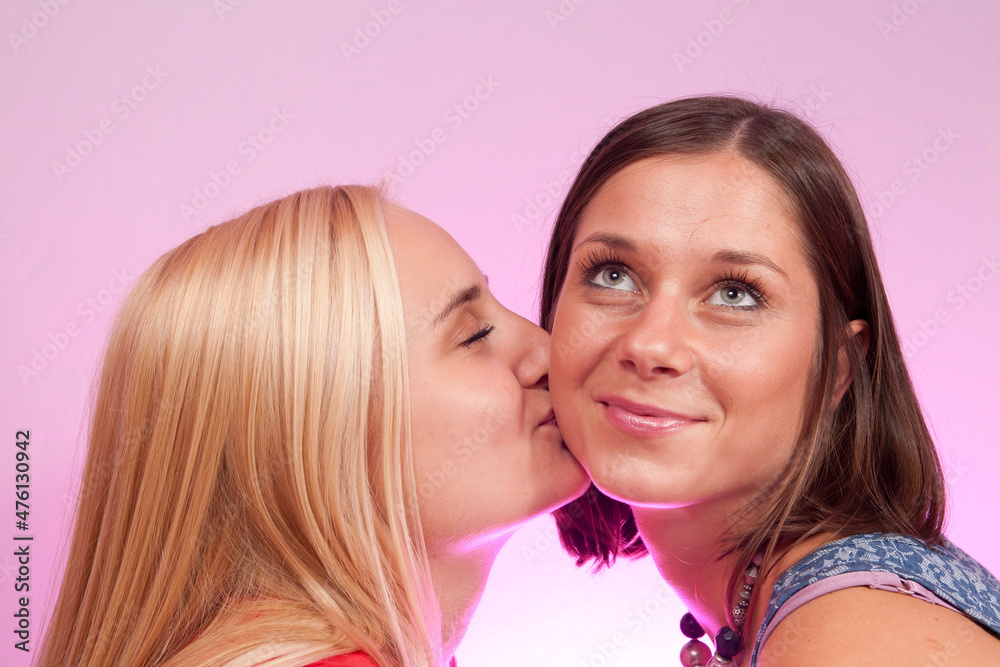 A brunette kissing another blonde girl on the cheek A brunette kissing another blonde girl on the cheek