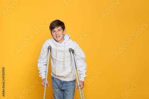 Teenage boy with injured leg using crutches on yellow background, space for text