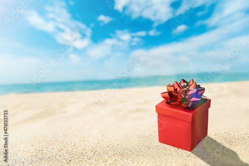Beautiful gift box with a ribbon standing on the sand with blue sea and sun on background.