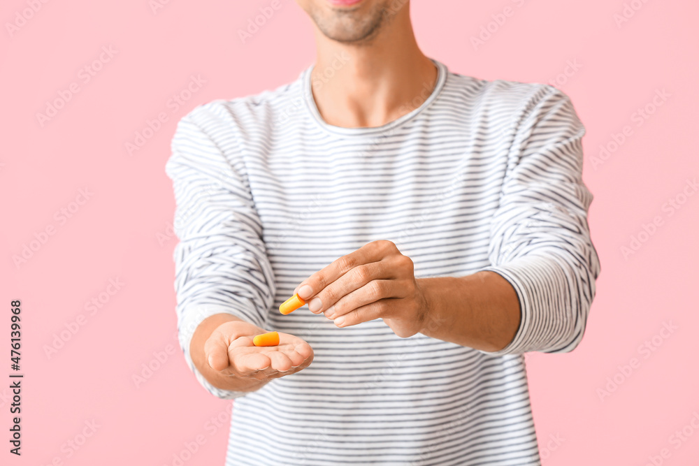 Young man with yellow ear plugs on pink background