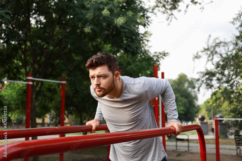 Fototapeta premium Young man doing pull-up on sport ground