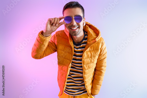 Stylish young man in sunglasses and yellow jacket on color background