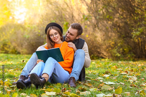 Loving couple sitting on green grass and reading book in autumn park