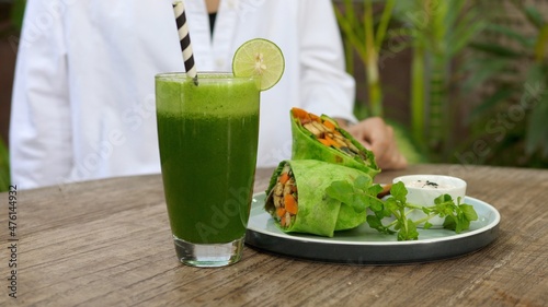 Person puts fresh kale and spinach green juice on the wooden table next to plant based pita. Clean eating concept