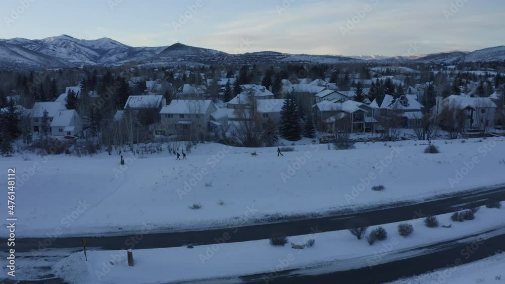 Drone view flying over thick layers of snow by the side of the road around Park City in Utah during winter. People walking back home at sunset with hills in the background. Drone view flying over thick layers of snow by the side of the road around Park City in Utah during winter. People walking back home at sunset with hills in the background.