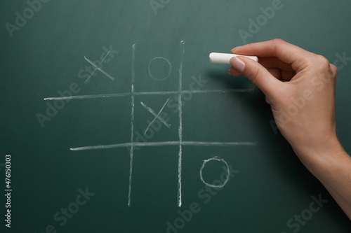 Woman playing tic tac toe game on green chalkboard, top view