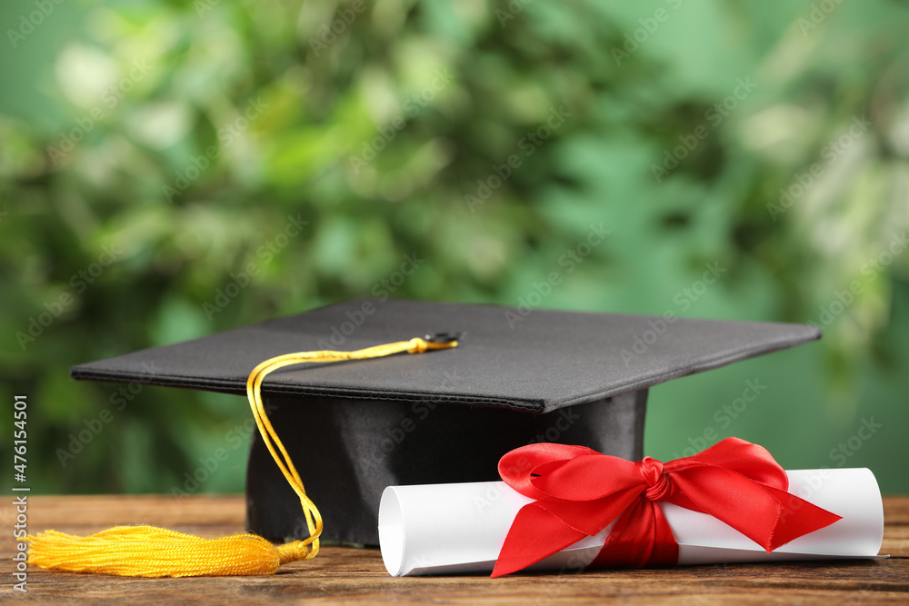 Graduation hat and diploma on wooden table against blurred background ...