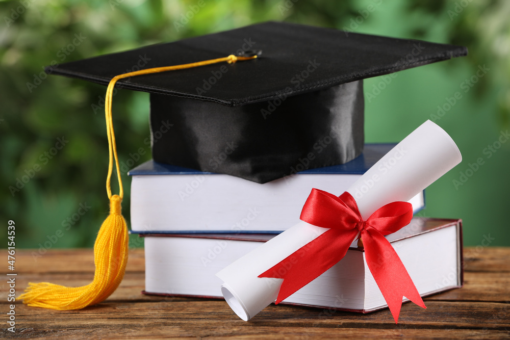 Graduation hat, books and diploma on wooden table against blurred background - obrazy, fototapety, plakaty 