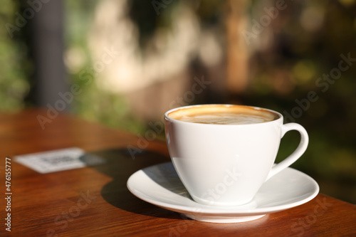 Cup of aromatic coffee with foam on table in outdoor cafe. Space for text