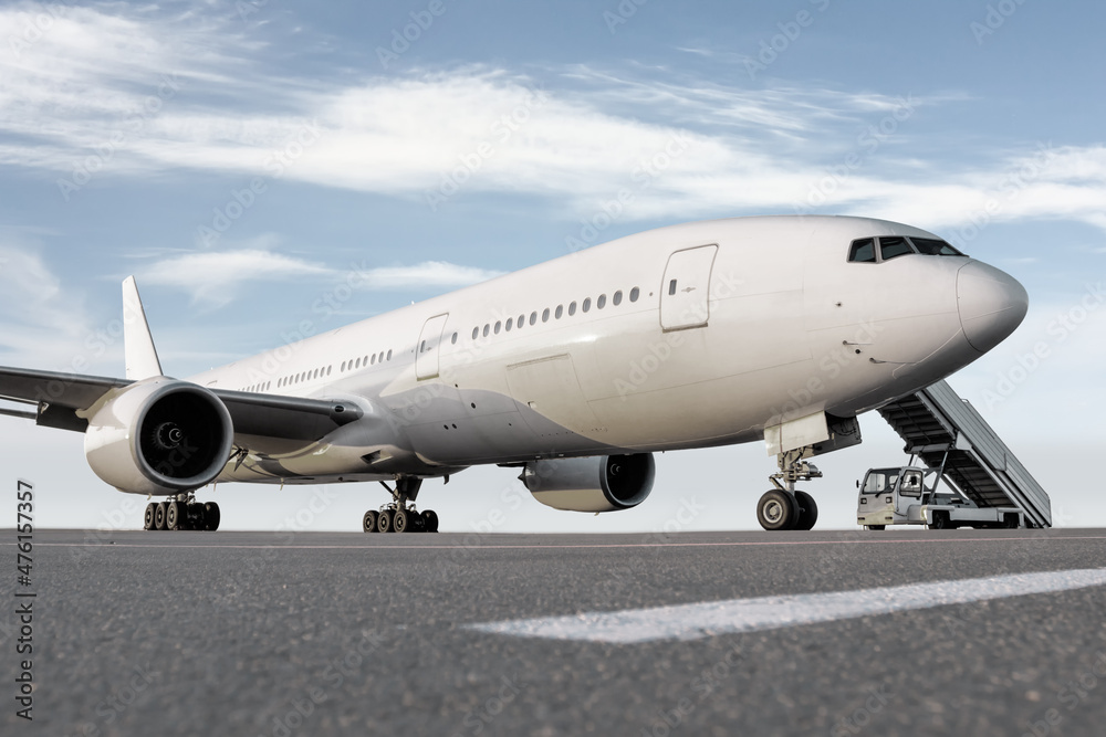 Wide body passenger airliner with a boarding stairs at the airport apron against the background of a bright sky Wide body passenger airliner with a boarding stairs at the airport apron against the background of a bright sky