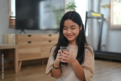 Cheerful young woman smiling and holding glass of fresh water .