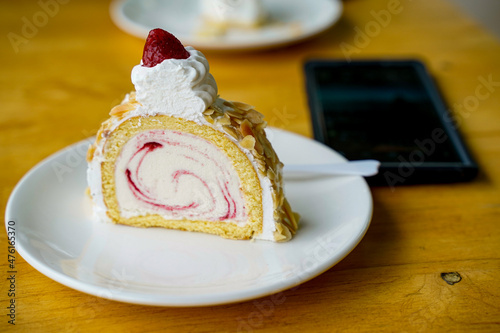 Almond strawberry roll desert servce on table next to mobile phone in cafe restaurant.Topping with strawberry on white plate. photo