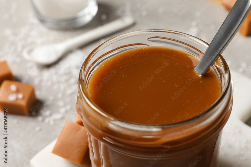 Tasty salted caramel and spoon in glass jar on table, closeup Tasty salted caramel and spoon in glass jar on table, closeup