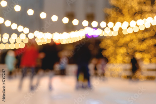 People ride skating rink on background of christmas tree in light garland. Blurred image. Wallpaper © svitlini