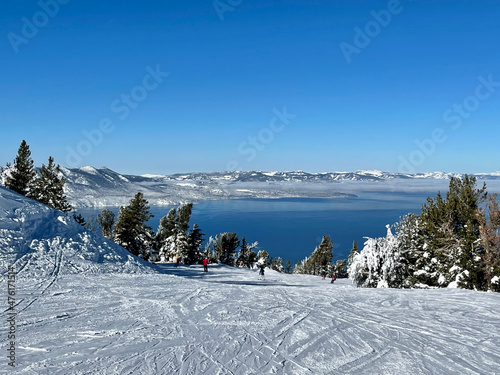 Scenic view of skiers and snowboarders on the slopes of a ski resort on a bluebird winter day, with Lake Tahoe in the background