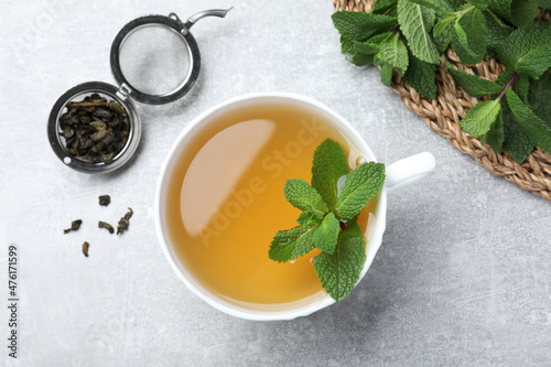 Cup of aromatic green tea with mint and dry leaves on grey table, flat lay
