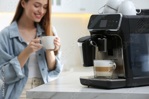 Fotografia Young woman enjoying fresh aromatic coffee in kitchen, focus on modern machine