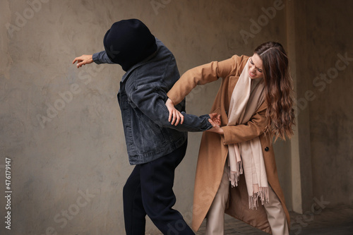 Woman defending herself from attacker near beige wall outdoors