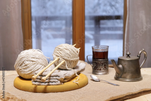 A woolen threads and knits, glass of tea on the table in front of the window on the background of winter landscape.