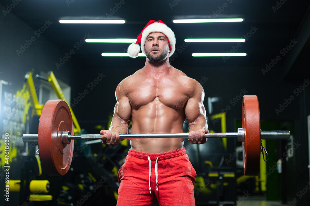 Front view of a sexy muscular man wearing Christmas hat and red shorts lifting a barbell in a gym Front view of a sexy muscular man wearing Christmas hat and red shorts lifting a barbell in a gym