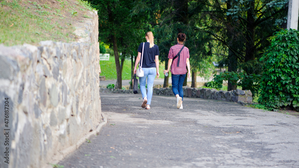 a pair of young girls. Back view of two attractive fitness girls going on a jogging in a public park. girlfriends or sisters are walking in the park, in the fresh air. Lifestyle.