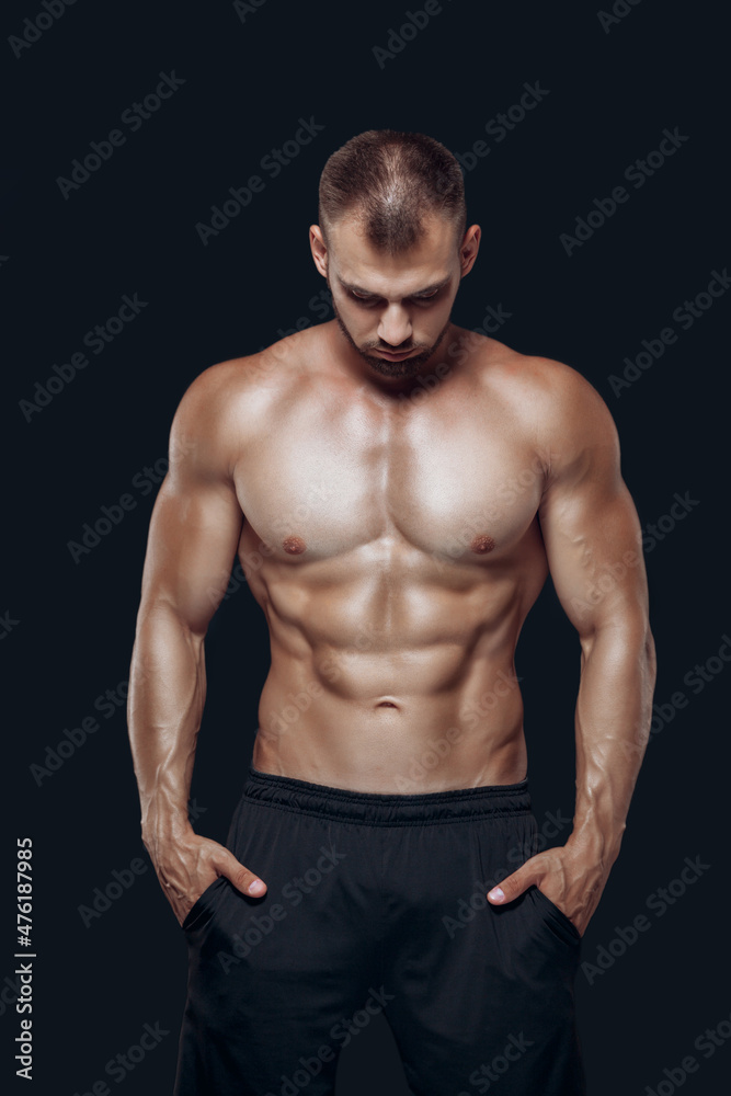 Muscular and fit young bodybuilder fitness male model posing standing with his head down over black background