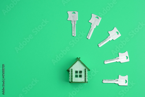 Conceptual composition: wooden model of a house and house keys on a colored background. Buying, selling, renting real estate. Top view, flat lay. © Natalya