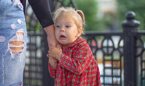 Canvas Print Caucasian little girl of 2 years with scared face holding hand of mother in summ