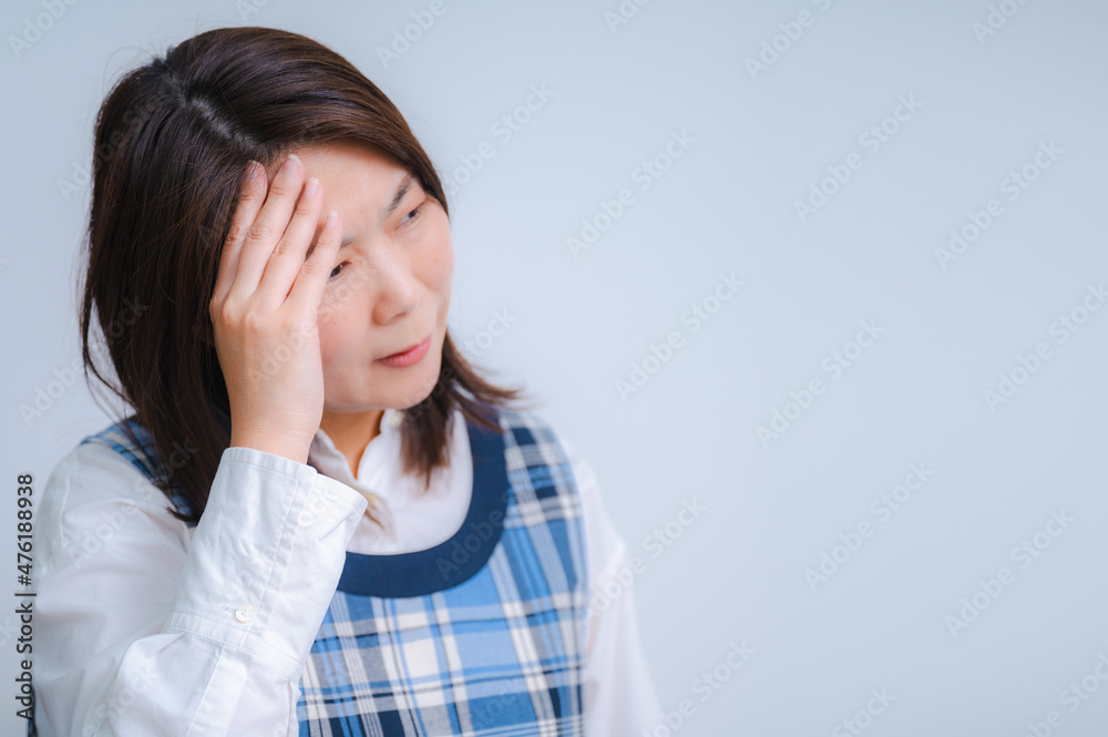 Image of a middle-class Japanese woman, housewife, touching her head for a headache Image of a middle-class Japanese woman, housewife, touching her head for a headache