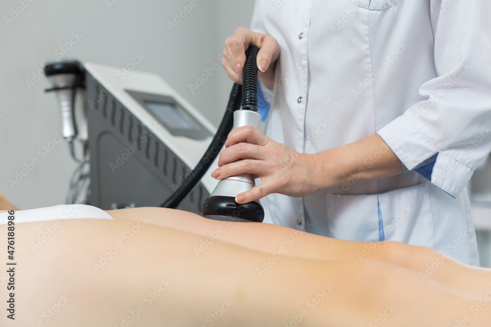 Slender woman receives a cavitation procedure getting anti-cellulite and anti-fat therapy on her tight buttocks in a beauty salon for splitting fat cells under the influence of ultrasound from a