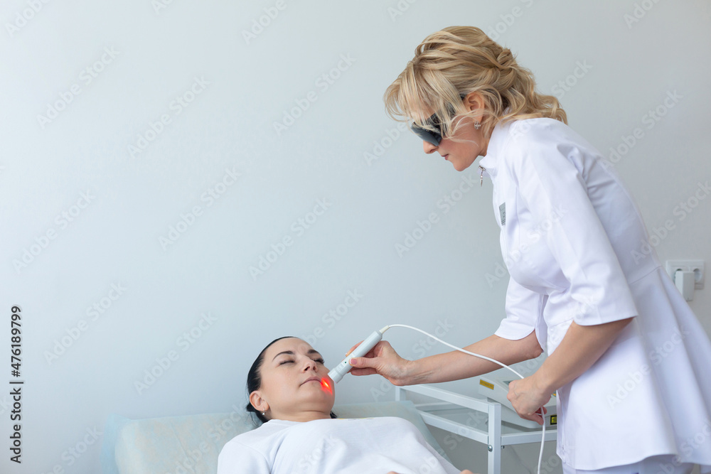 The use of a laser therapeutic device by a dermatologist during a cosmetic rejuvenation procedure in the clinic The use of a laser therapeutic device by a dermatologist during a cosmetic rejuvenation procedure in the clinic