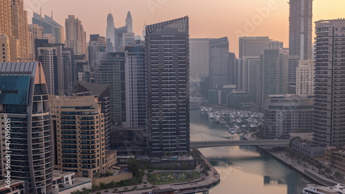Dubai Marina with several boats and yachts parked in harbor and skyscrapers around canal aerial morning timelapse.
