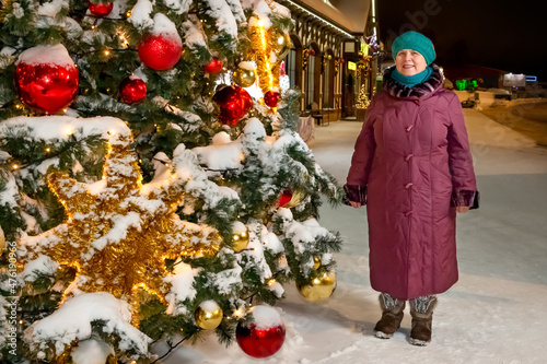 An elderly woman on the street by the Christmas tree.