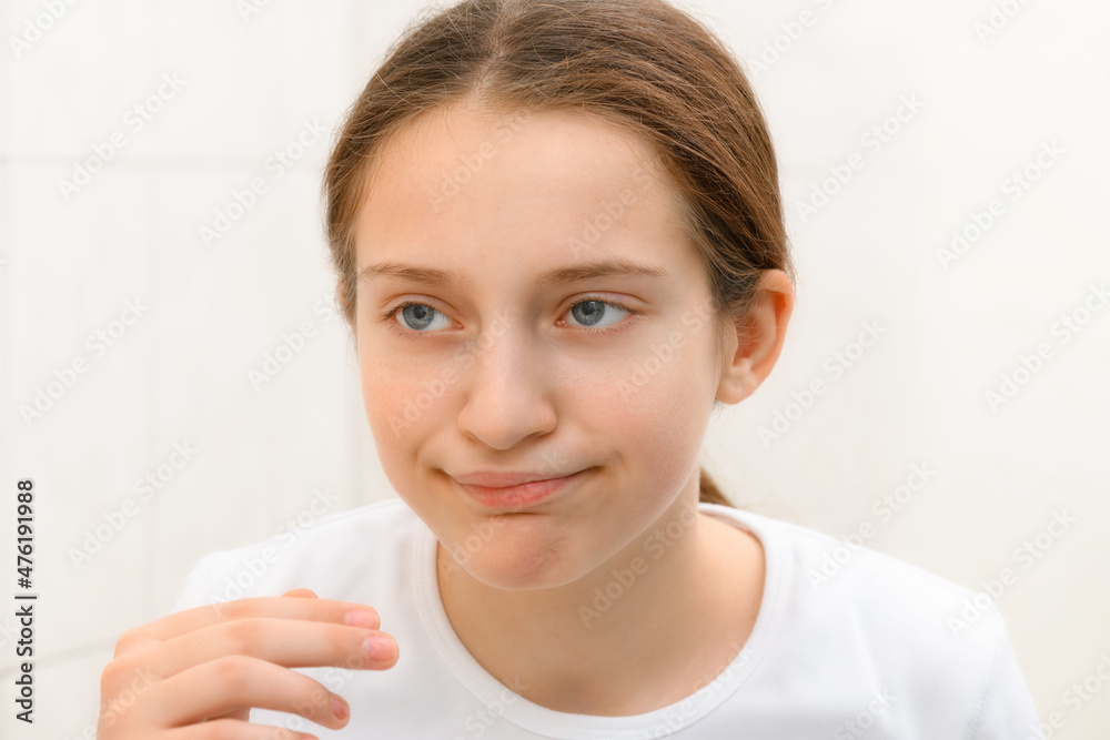 face of teenage girl, she looks at herself in the mirror and touches her face with her hand, she is upset and has frustrated emotions face of teenage girl, she looks at herself in the mirror and touches her face with her hand, she is upset and has frustrated emotions