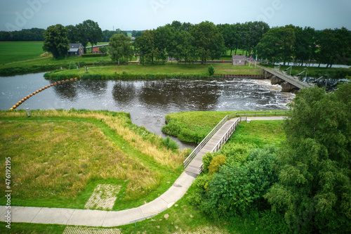 Drone view of the river Vecht, green grass, trees, beautiful blue sky and cycle path through the Vecht valley. Bridge and weir in the river. Dalfsen Netherlands