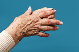 A senior woman massages her fingers, experiencing pain in the joints. The diseased joints are highlighted in red. Blue background, hands close-up. The concept of rheumatism and arthritis