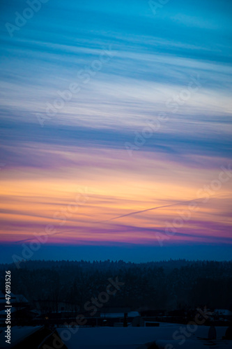 Bright evening sky in Lithuania. Orange and blue cloudscape, dusk illuminating the clouds. Dark forest in the foreground. Selective focus on the details, blurred background.