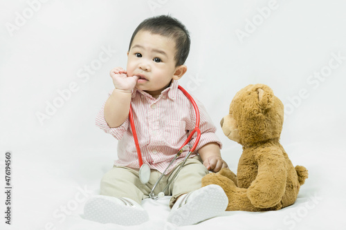 Adorable asian baby boy in pink shirt plays in doctor toy bear and red stethoscope.Health care and medical concept.