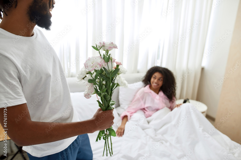 Man with bouquet of flowers near girlfriend in bed