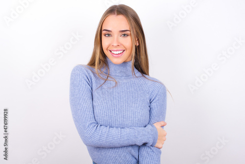 Young caucasian girl wearing blue turtleneck over white background laughing.