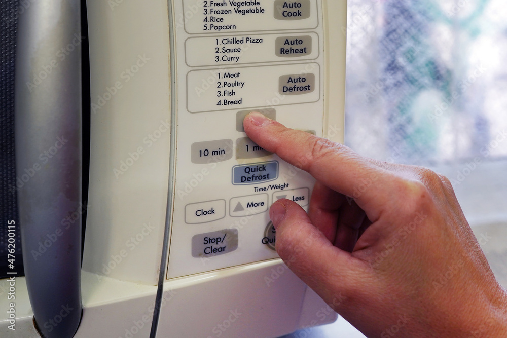 Hand pushing button of microwave oven for cooking food in kitchen. Close-up background of hand turning setting timer on microwave. Home cooking or food prepping concept Hand pushing button of microwave oven for cooking food in kitchen. Close-up background of hand turning setting timer on microwave. Home cooking or food prepping concept