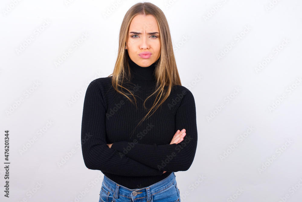 Picture of angry Young caucasian girl wearing black turtleneck over white background crossing arms. Looking at camera with disappointed expression. Picture of angry Young caucasian girl wearing black turtleneck over white background crossing arms. Looking at camera with disappointed expression.