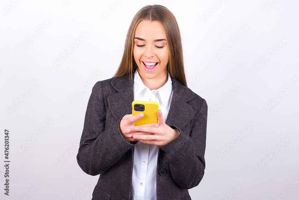 Smiling Young business woman wearing jacket over white background using cell phone, messaging, being happy to text with friends, looking at smartphone. Modern technologies and communication. Smiling Young business woman wearing jacket over white background using cell phone, messaging, being happy to text with friends, looking at smartphone. Modern technologies and communication.
