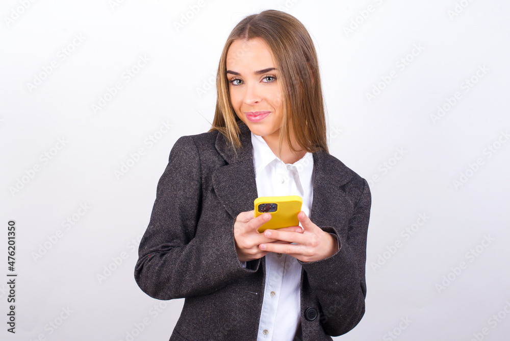 Happy Young business woman wearing jacket over white background listening to music with earphones using mobile phone. Happy Young business woman wearing jacket over white background listening to music with earphones using mobile phone.