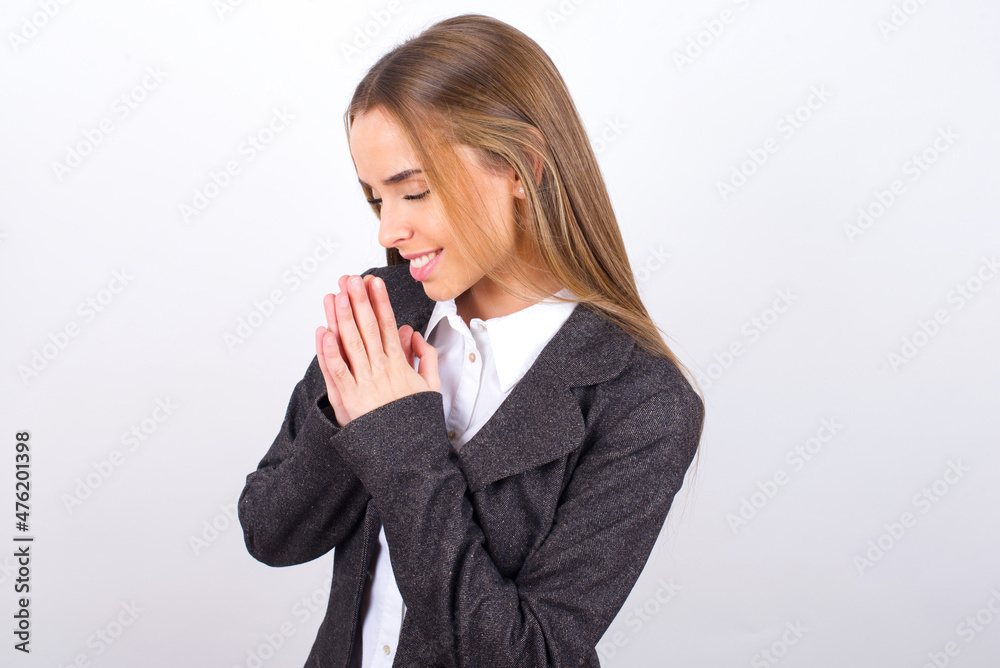 Overjoyed Young business woman wearing jacket over white background laughs joyfully and keeps palms pressed together hears something funny Overjoyed Young business woman wearing jacket over white background laughs joyfully and keeps palms pressed together hears something funny