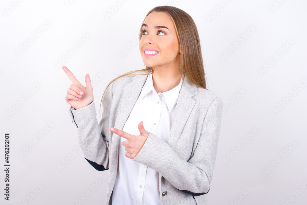 Optimistic Young business woman wearing jacket over white background points with both hands and looking at empty space. Optimistic Young business woman wearing jacket over white background points with both hands and looking at empty space.