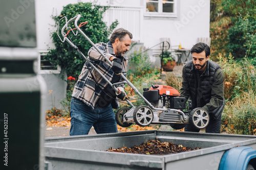 Father loading lawn mower with son in vehicle trailer photo