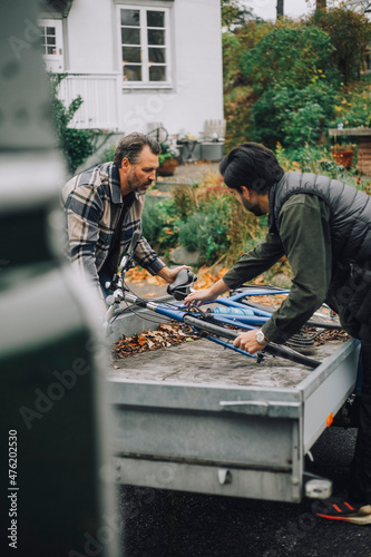 Son helping father to load bicycle in vehicle trailer photo